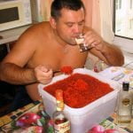 shirtless russian man eating tub of caviar